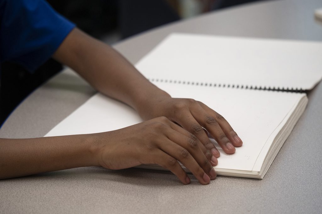 Photo of young person's hands reading braille. 