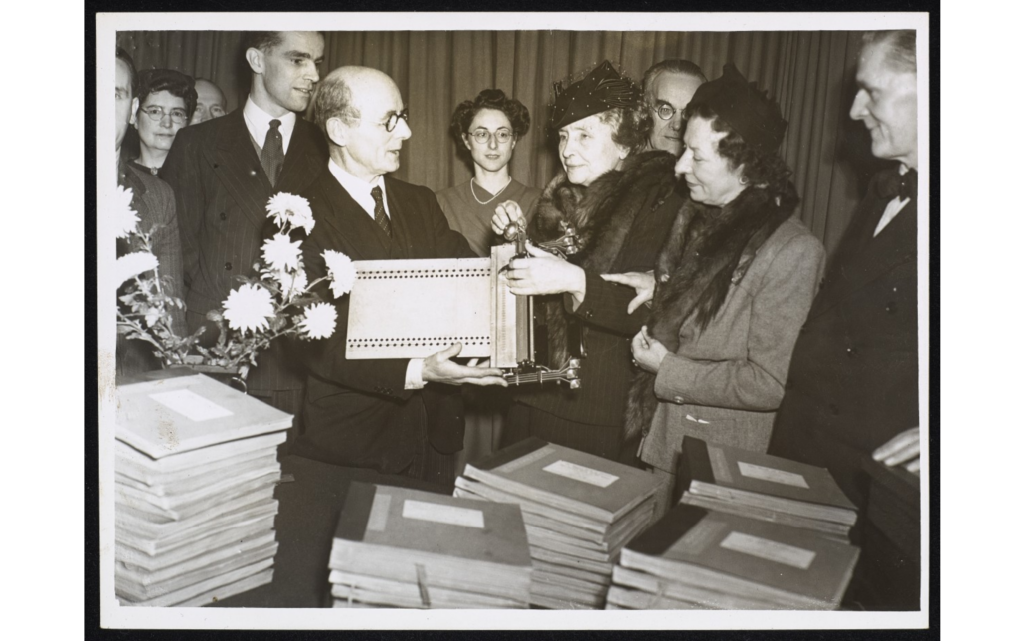 Helen Keller with a group of people reading braille on brailler at event 