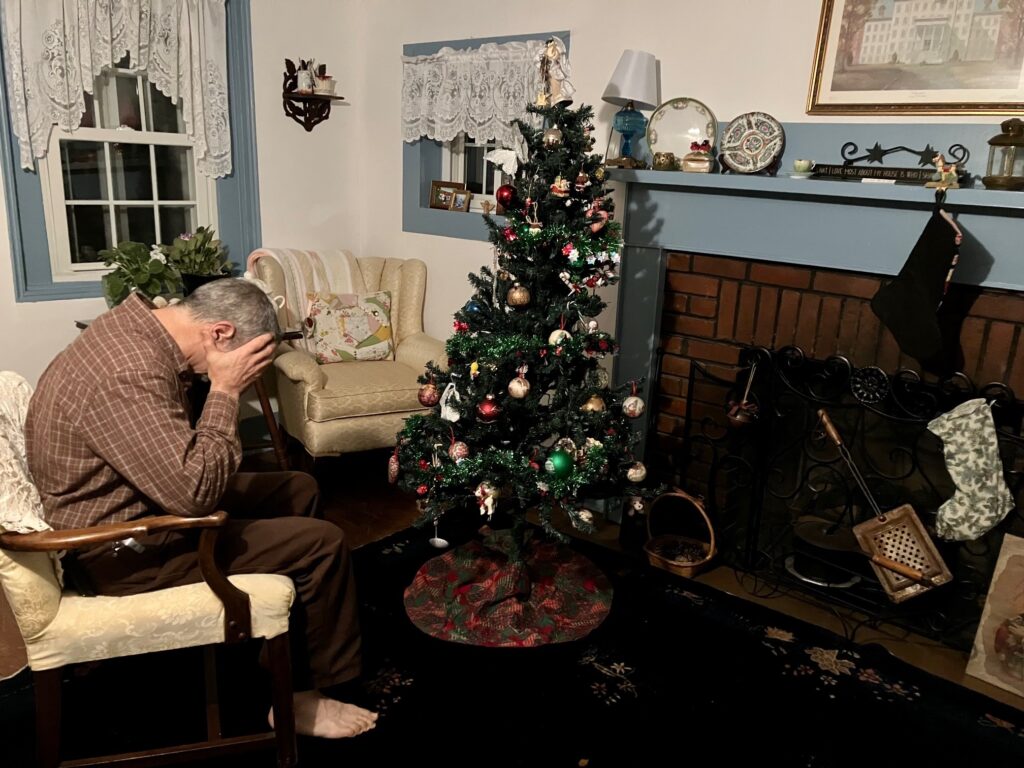 man with head in hands sitting by Christmas tree alone depicting depression during the holidays.
